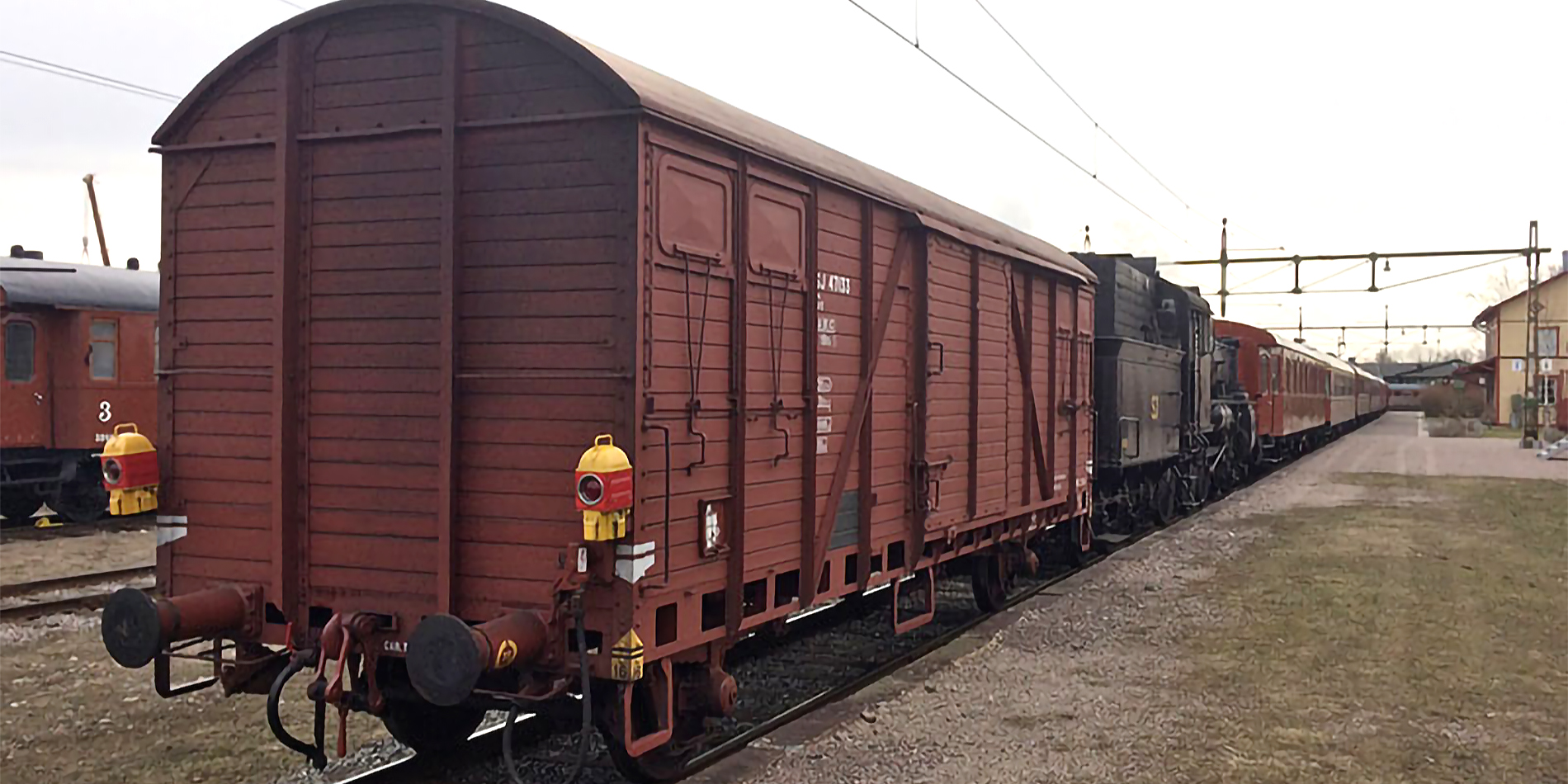 The rear end of a rust brown freight car with taillights standing at the end of the train at a station building.