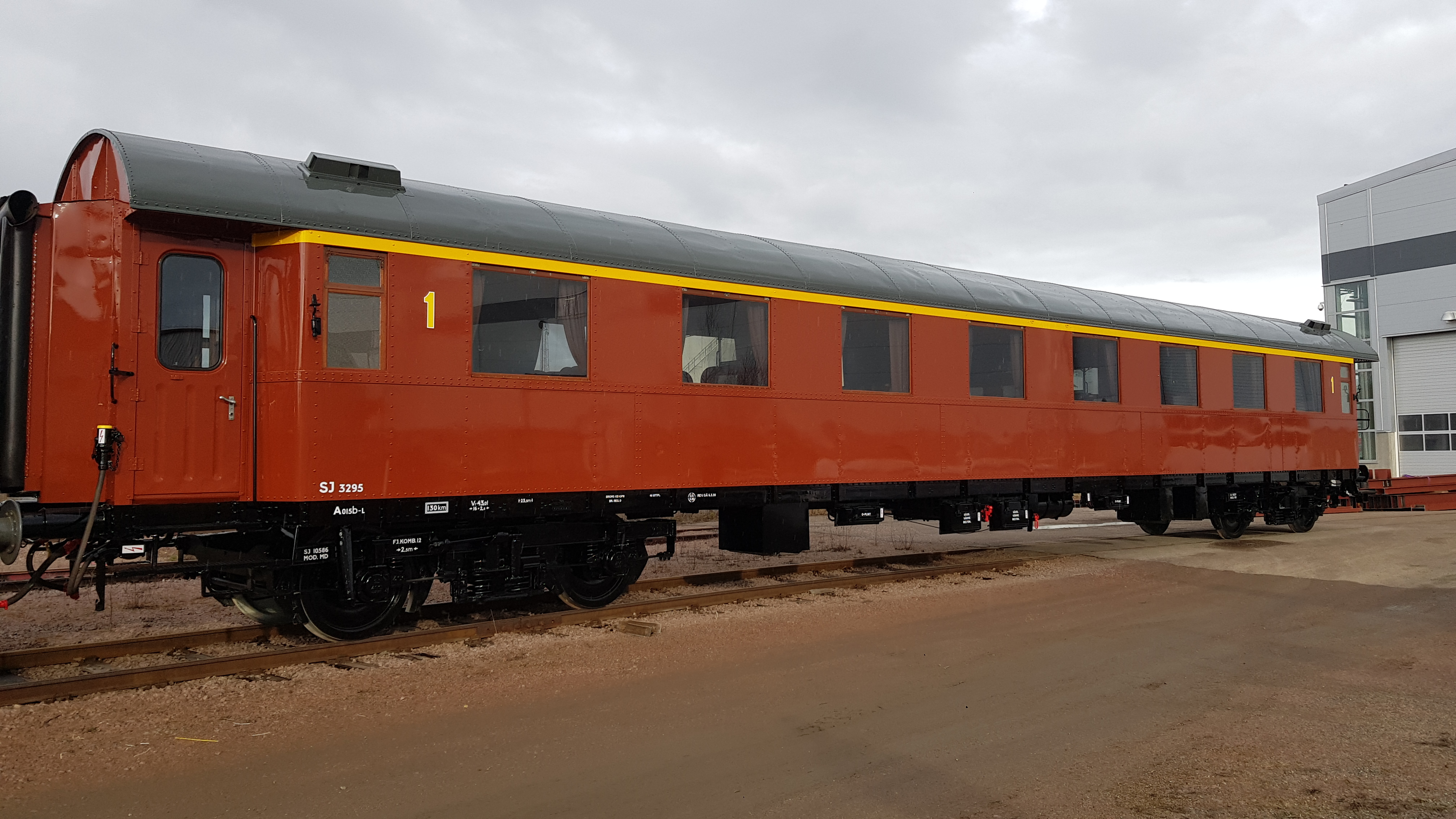 Rust red passenger car with yellow stripe above the windows placed on the track area.