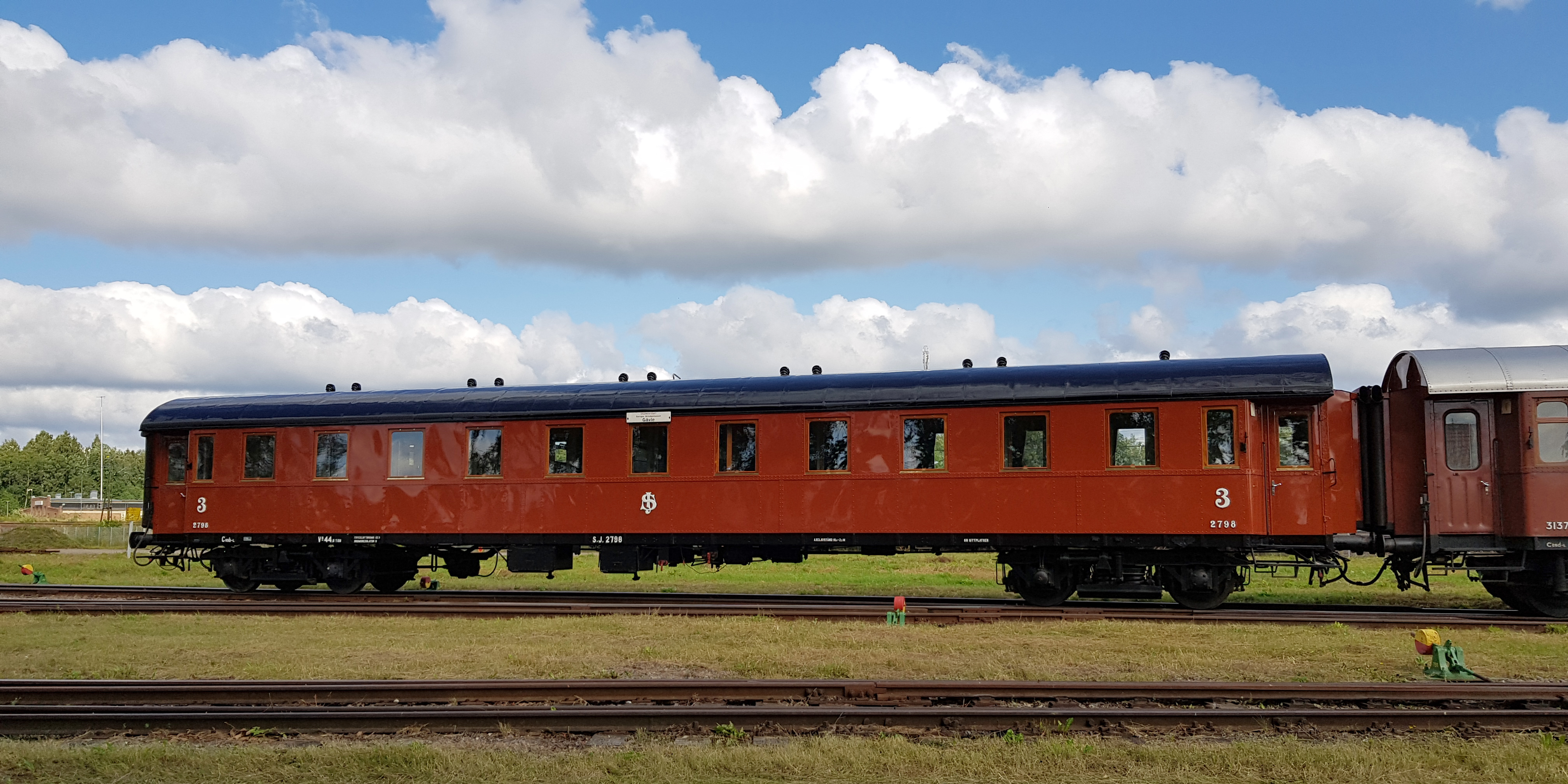 Rust red passenger car connected between other cars.
