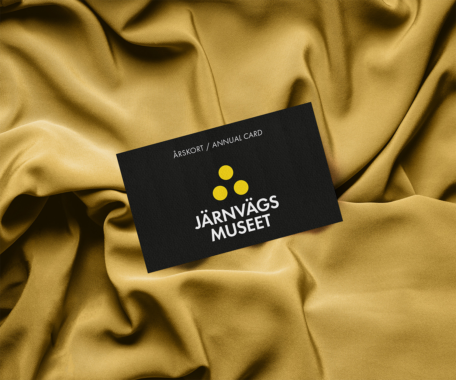 A black card with the museum logotype lays on a golden fabric.