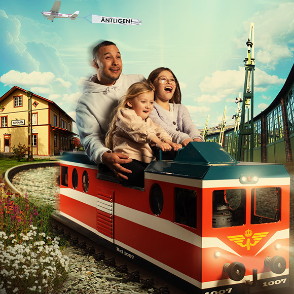 en man och två barn sitter i ett mini-tåg i en blomstrande miljö på Järnvägsmuseet
