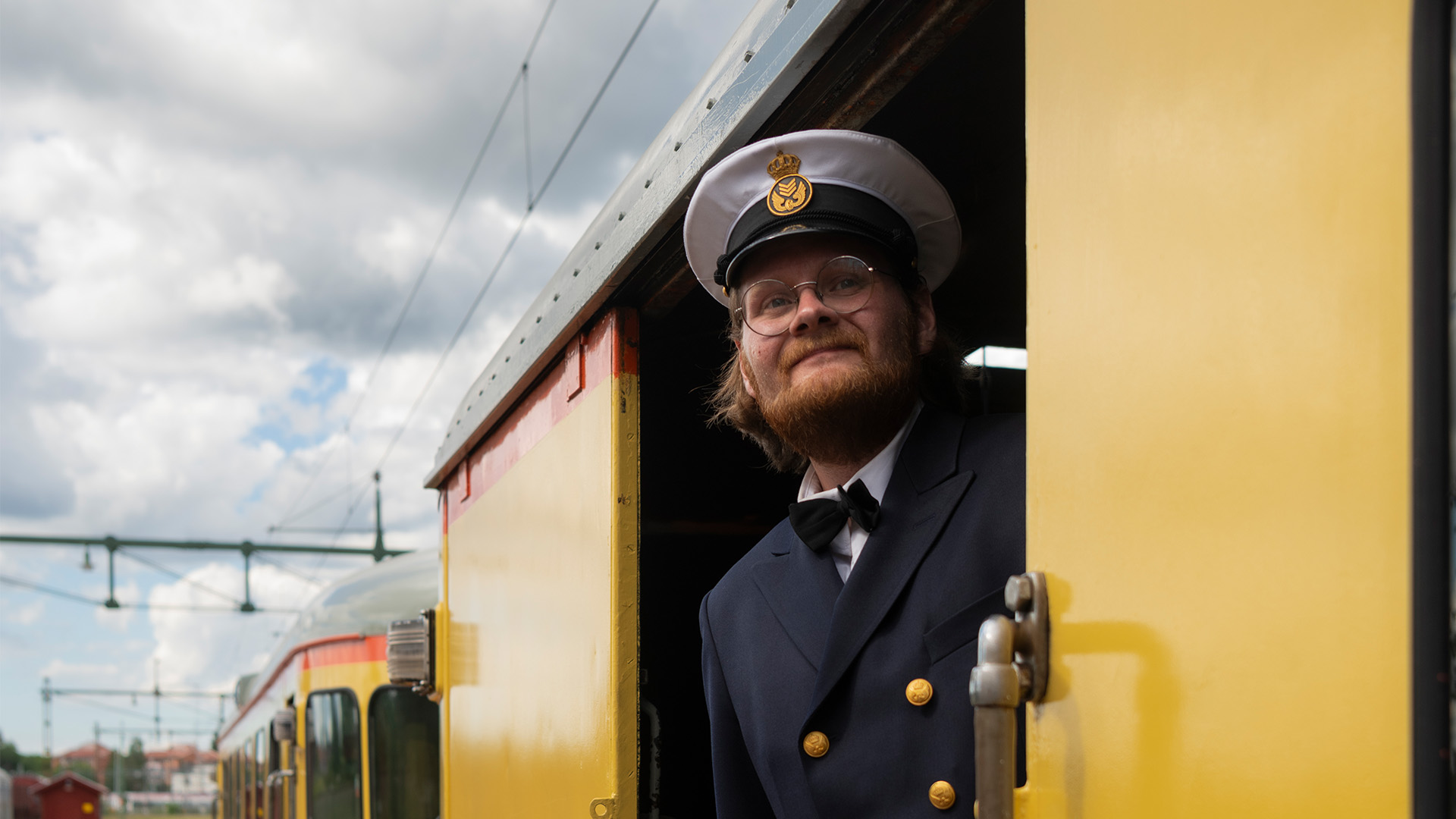 en man står ombord på en orange och gul rälsbuss och tittar ut mot perrongen