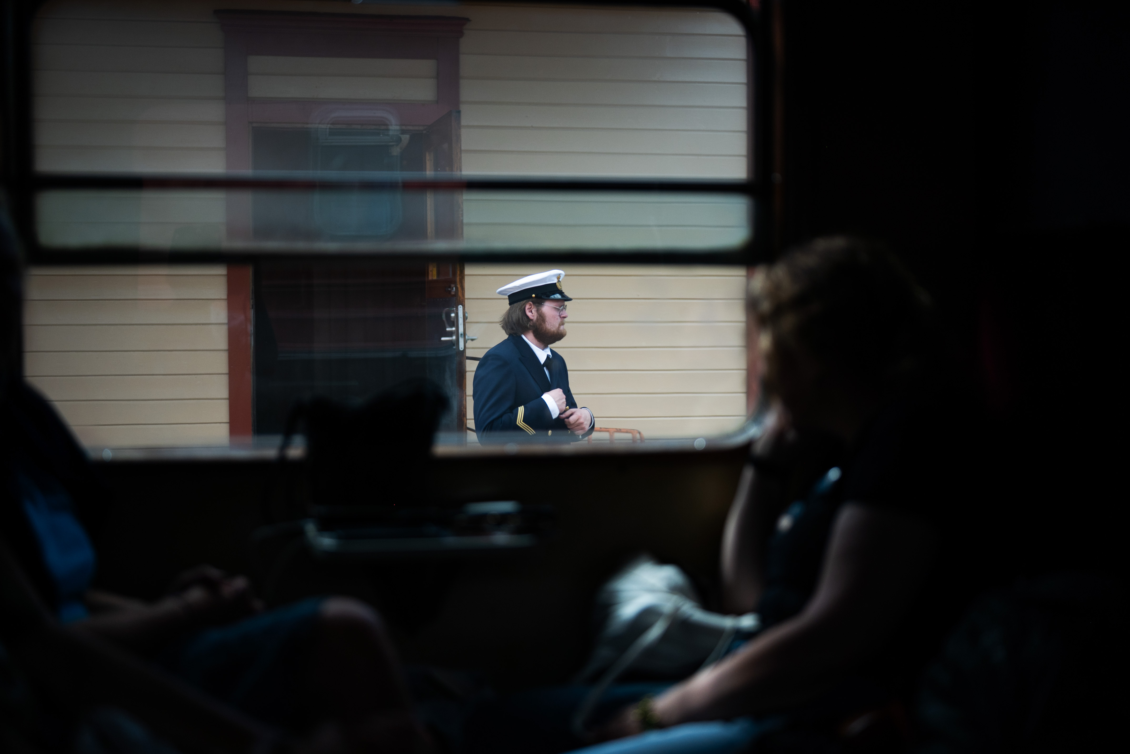Bilden är tagen i en tågvagn, genom ett stort tågfönster syns en man i uniform på perrongen.