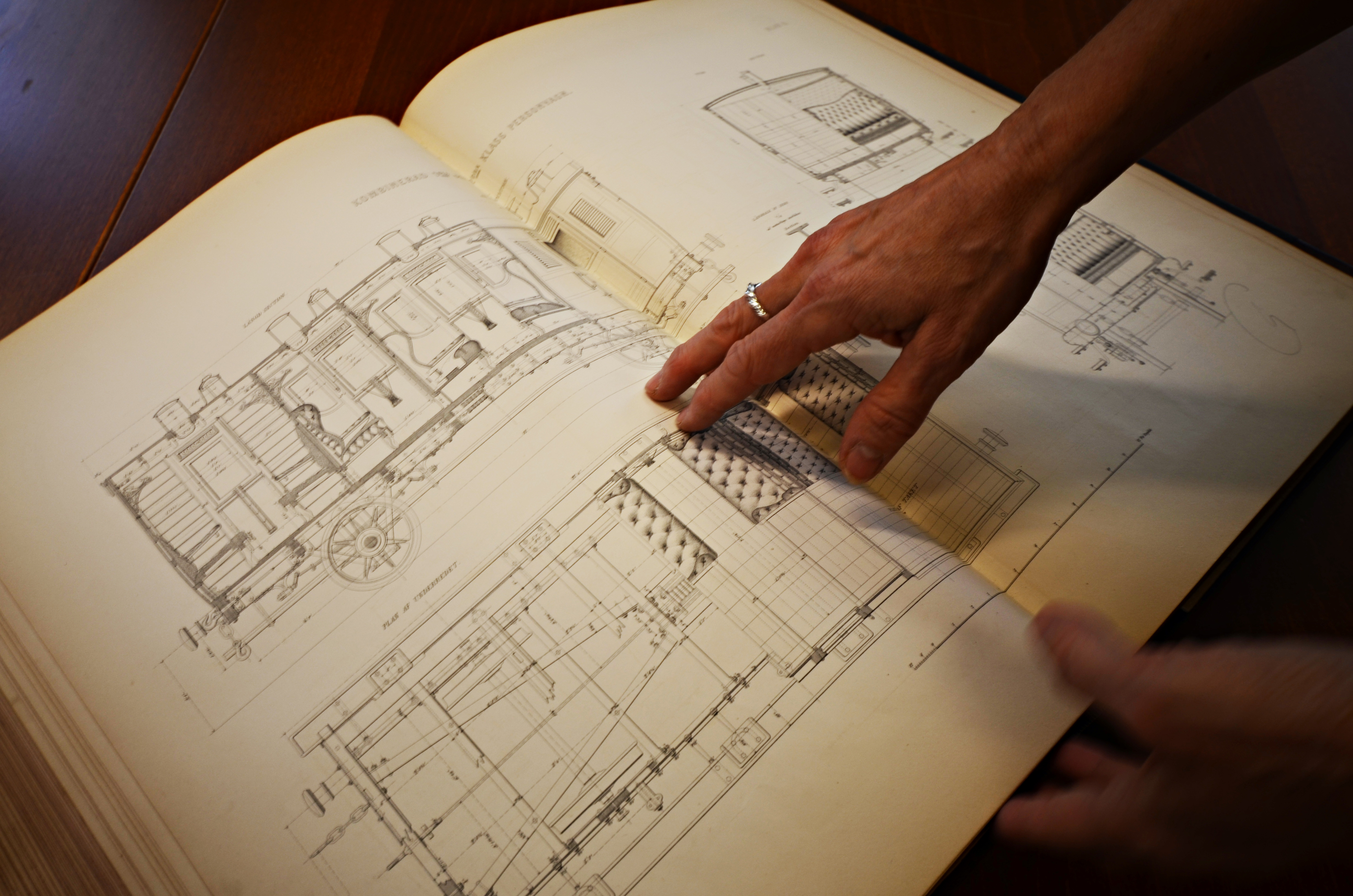 En närbild på en uppslagen inbunden bok med ritningar med en hand som håller ner uppslaget.