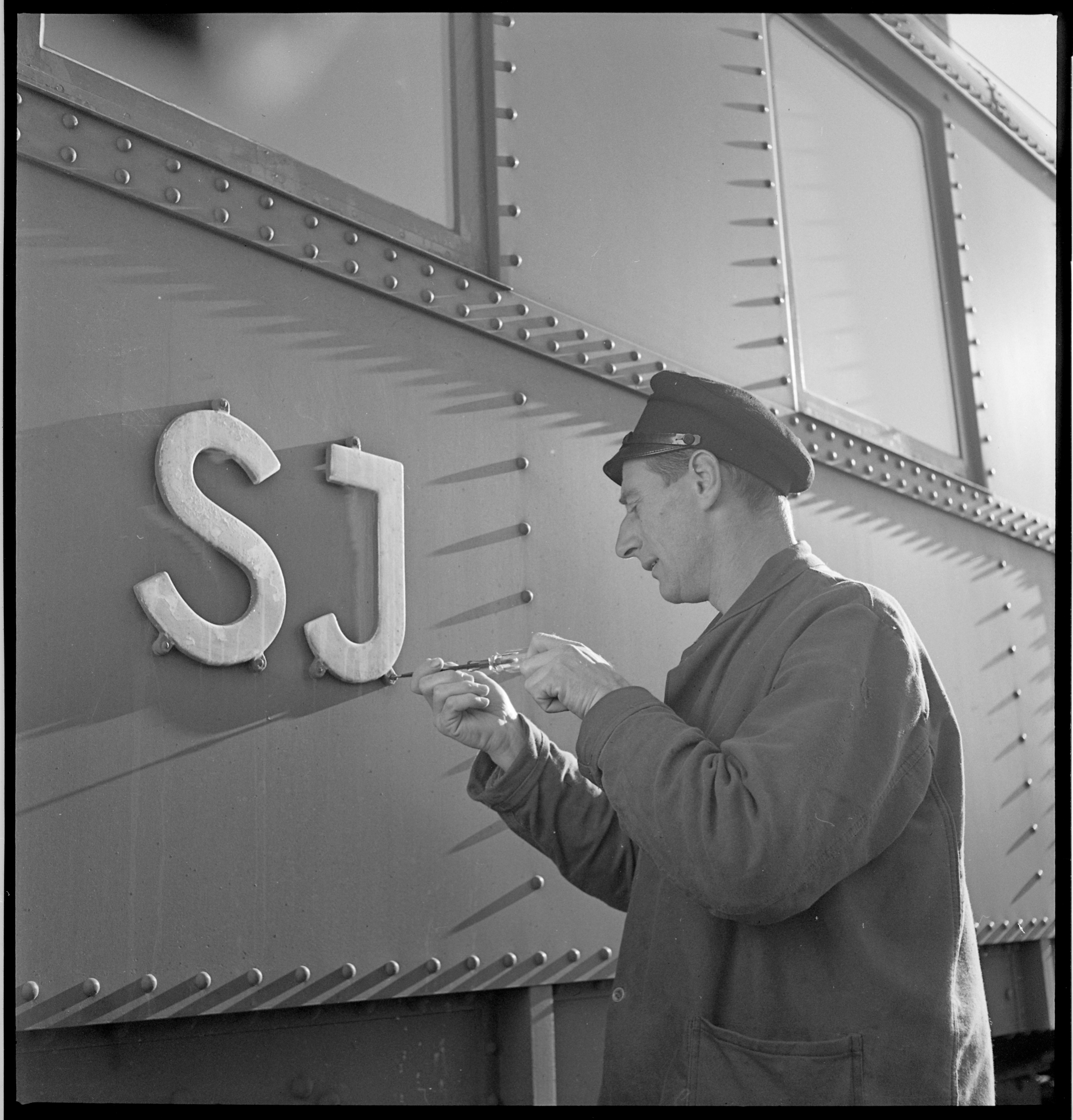 En man skruvar in en skylt med SJ på utsidan av en tågvagn.