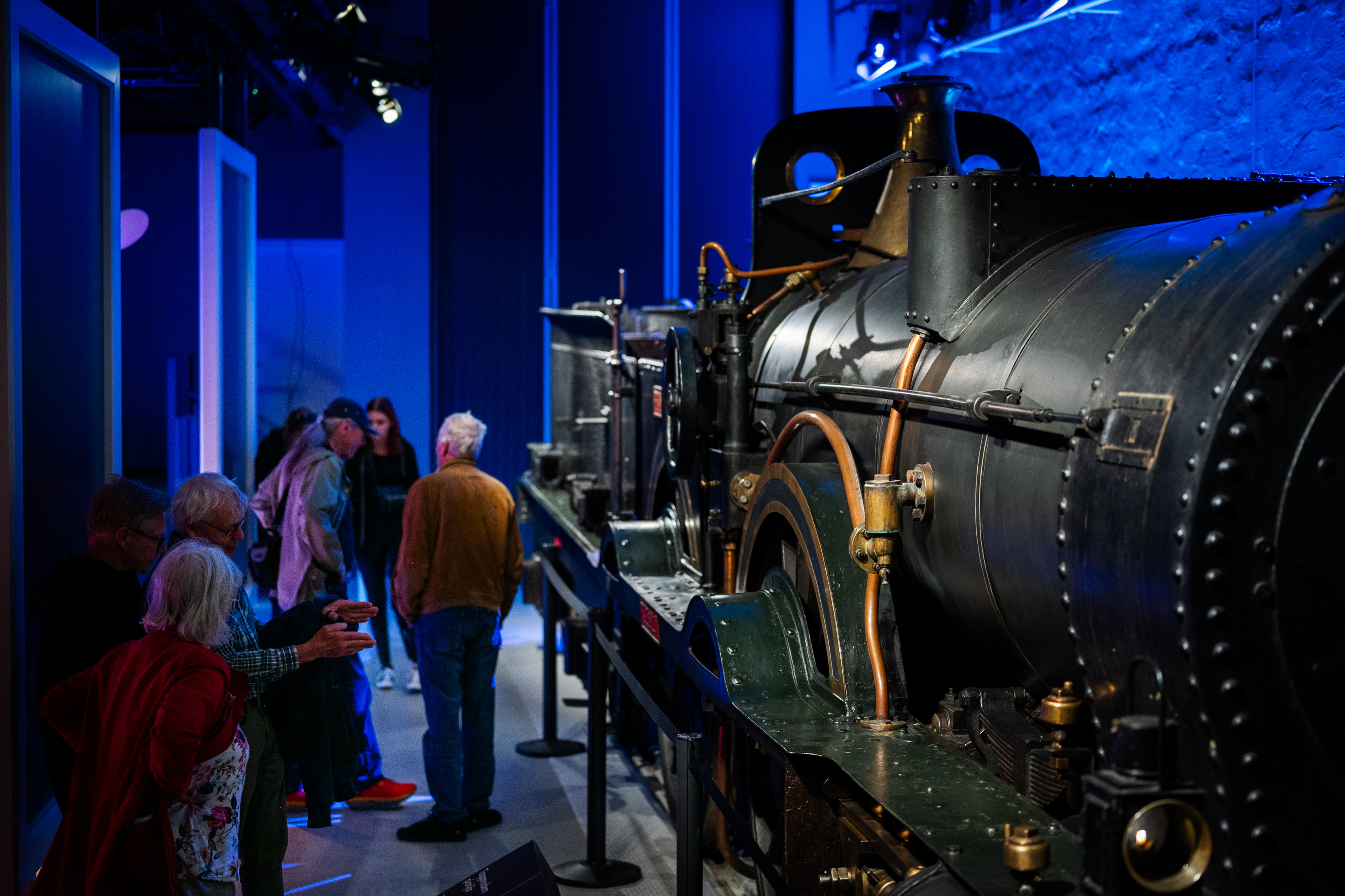 A group of people are standing in front of a big steam locomotive in a exhibition hall