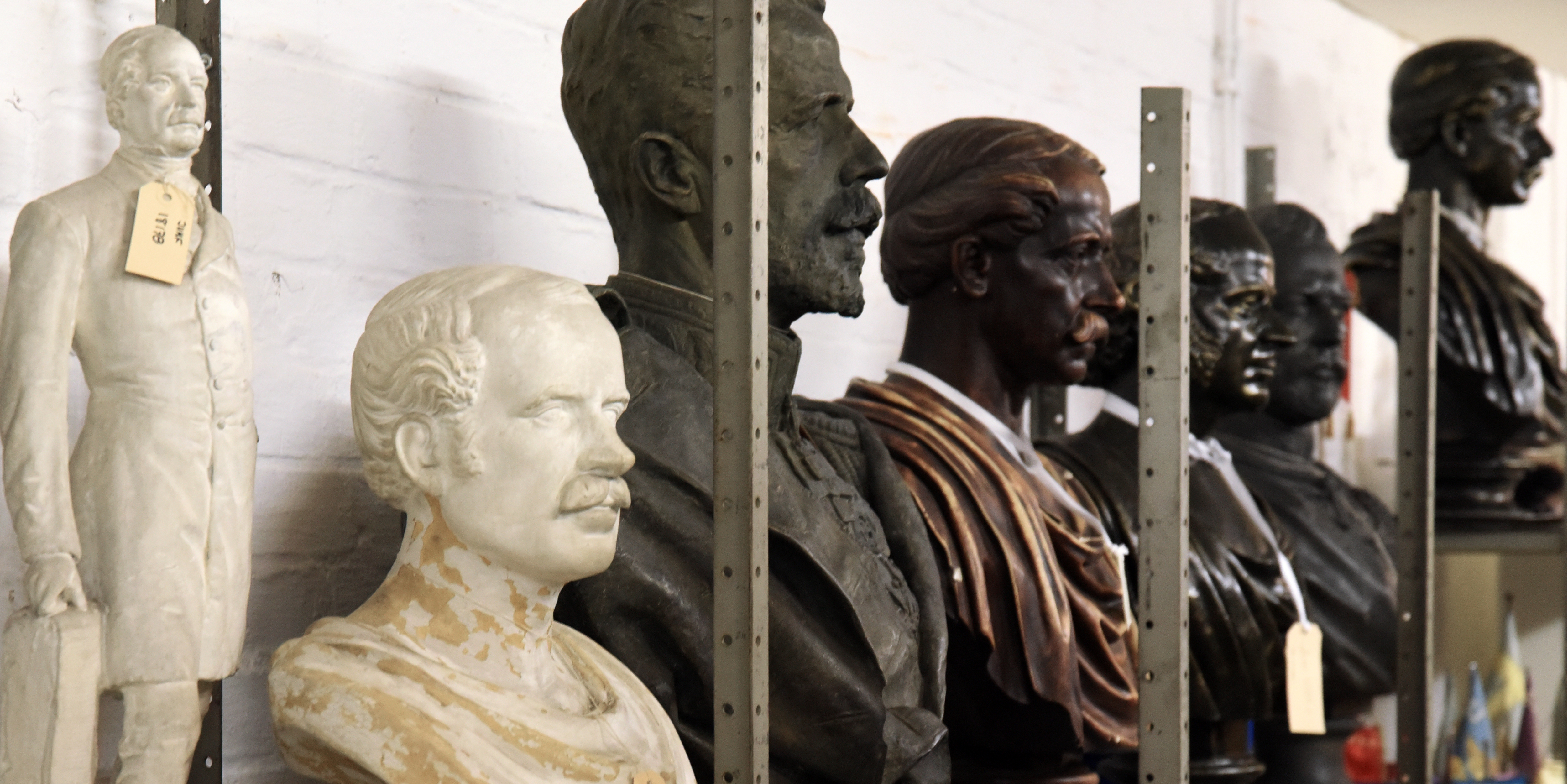 A row of busts of men on a warehouse shelf.