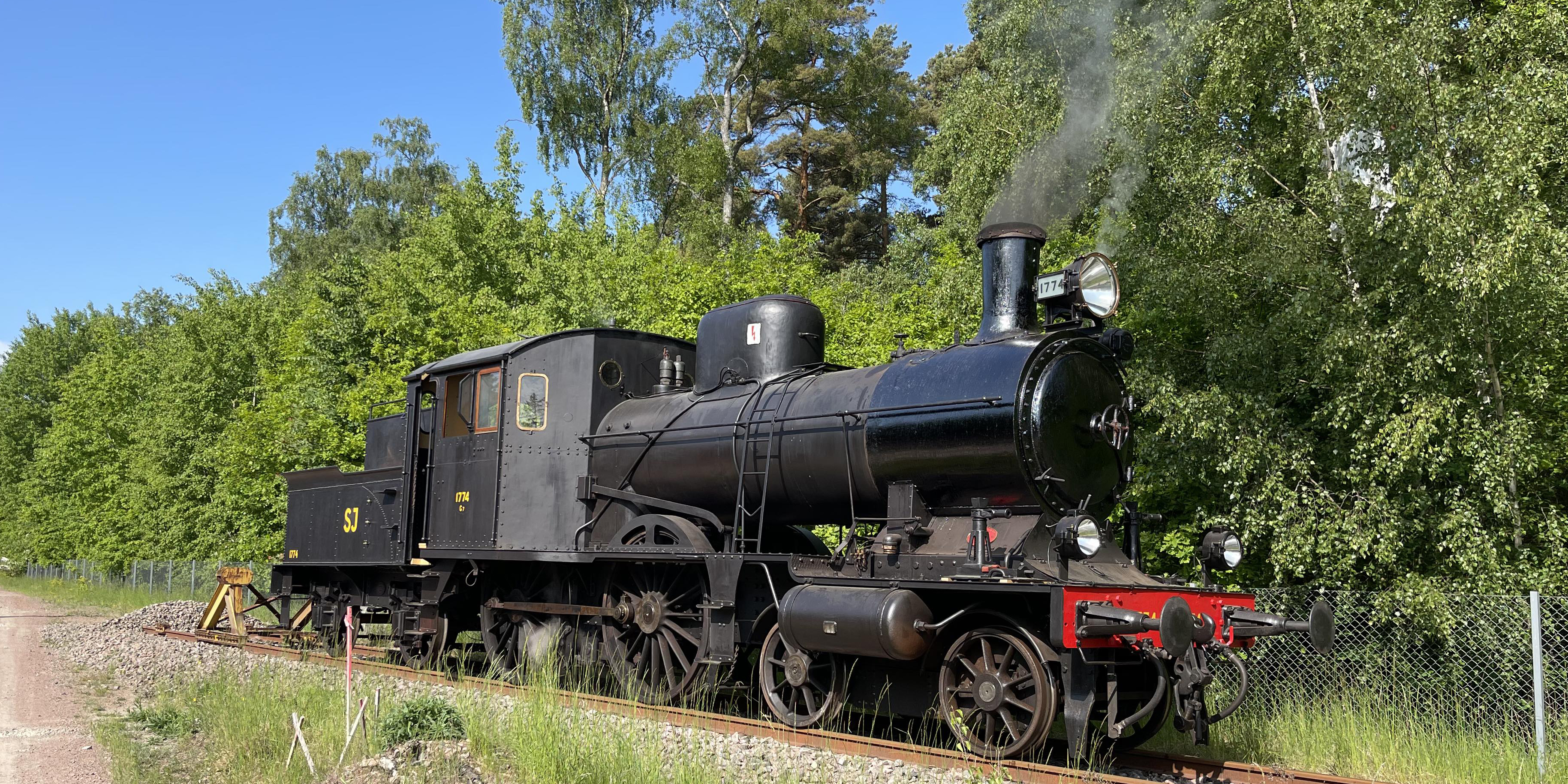 Svart lok stående på räls en grönskande sommardag.