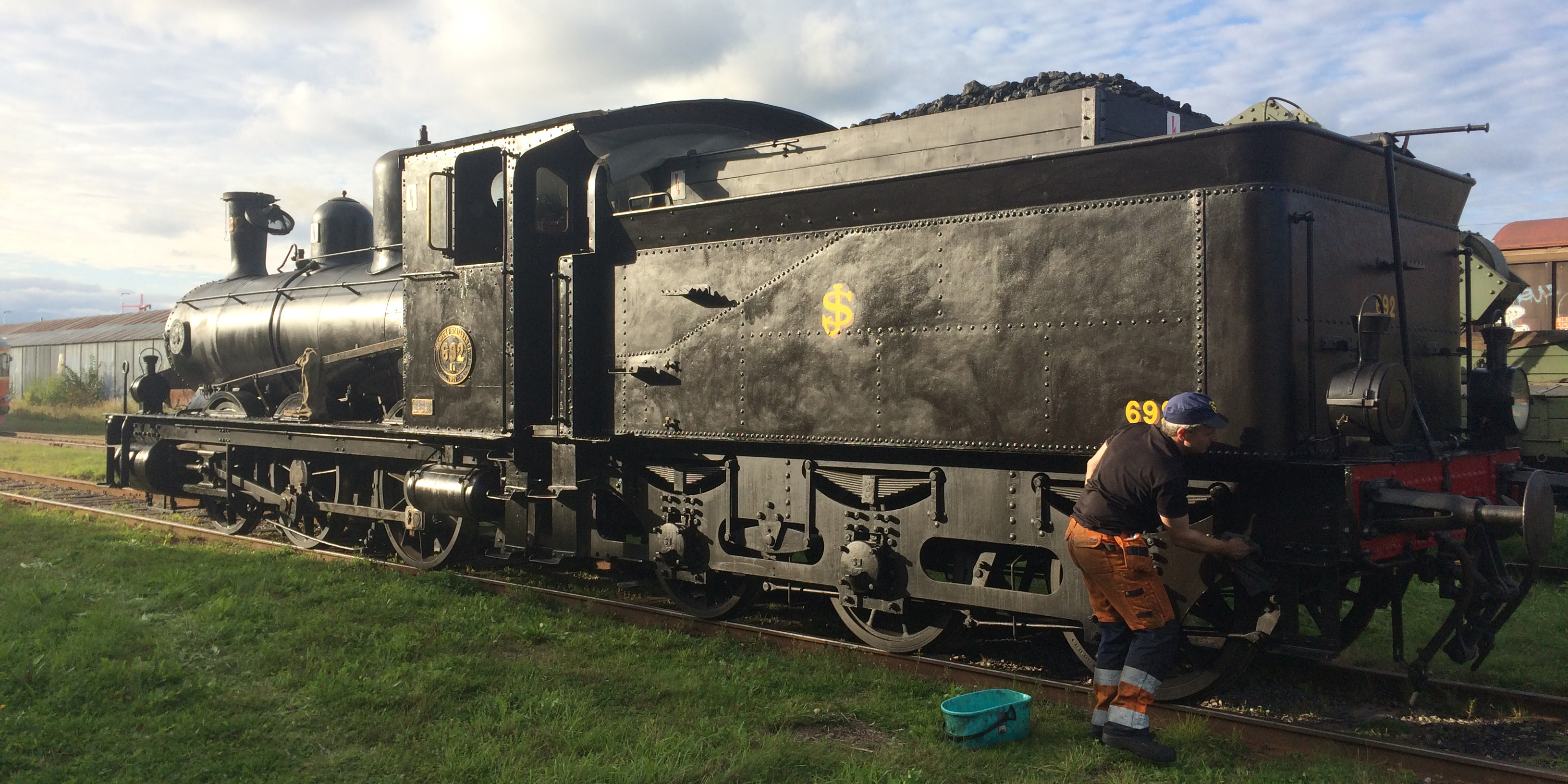 Locomotive with a lot of coal in the load standing on tracks. Men in work clothes are polishing the locomotive.