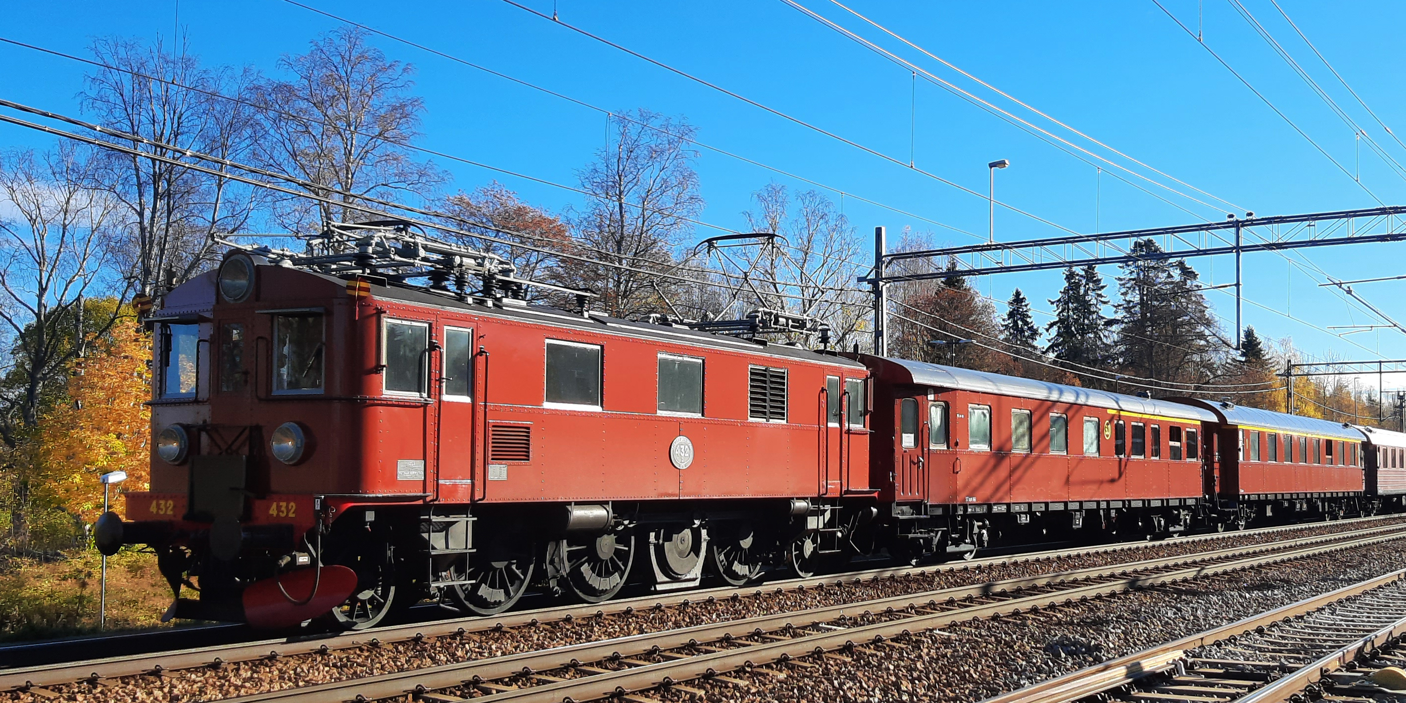 Red locomotive with red wagons on rails in autumn landscape.