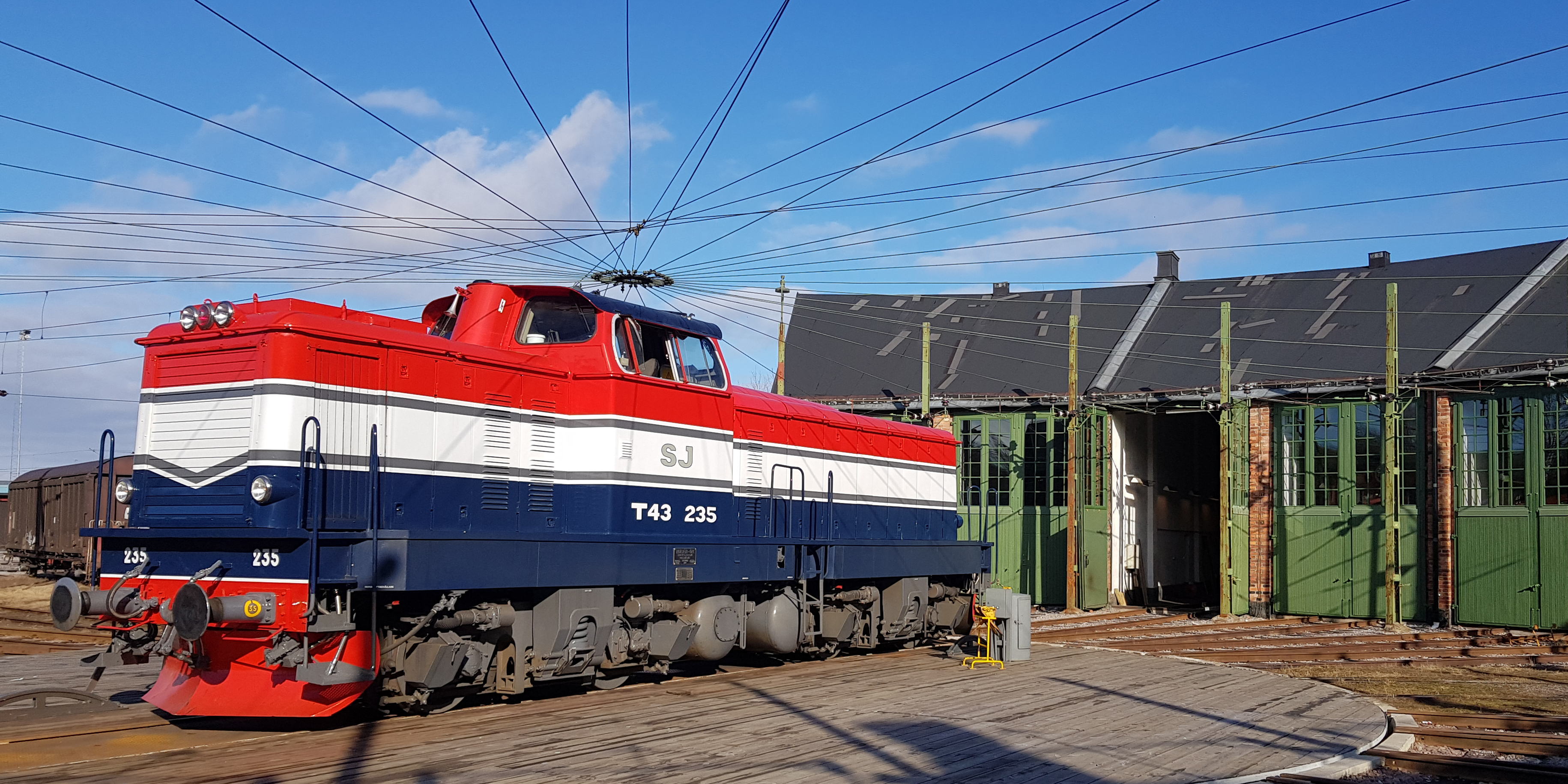 Locomotives in red, white and blue in front of a green round house.