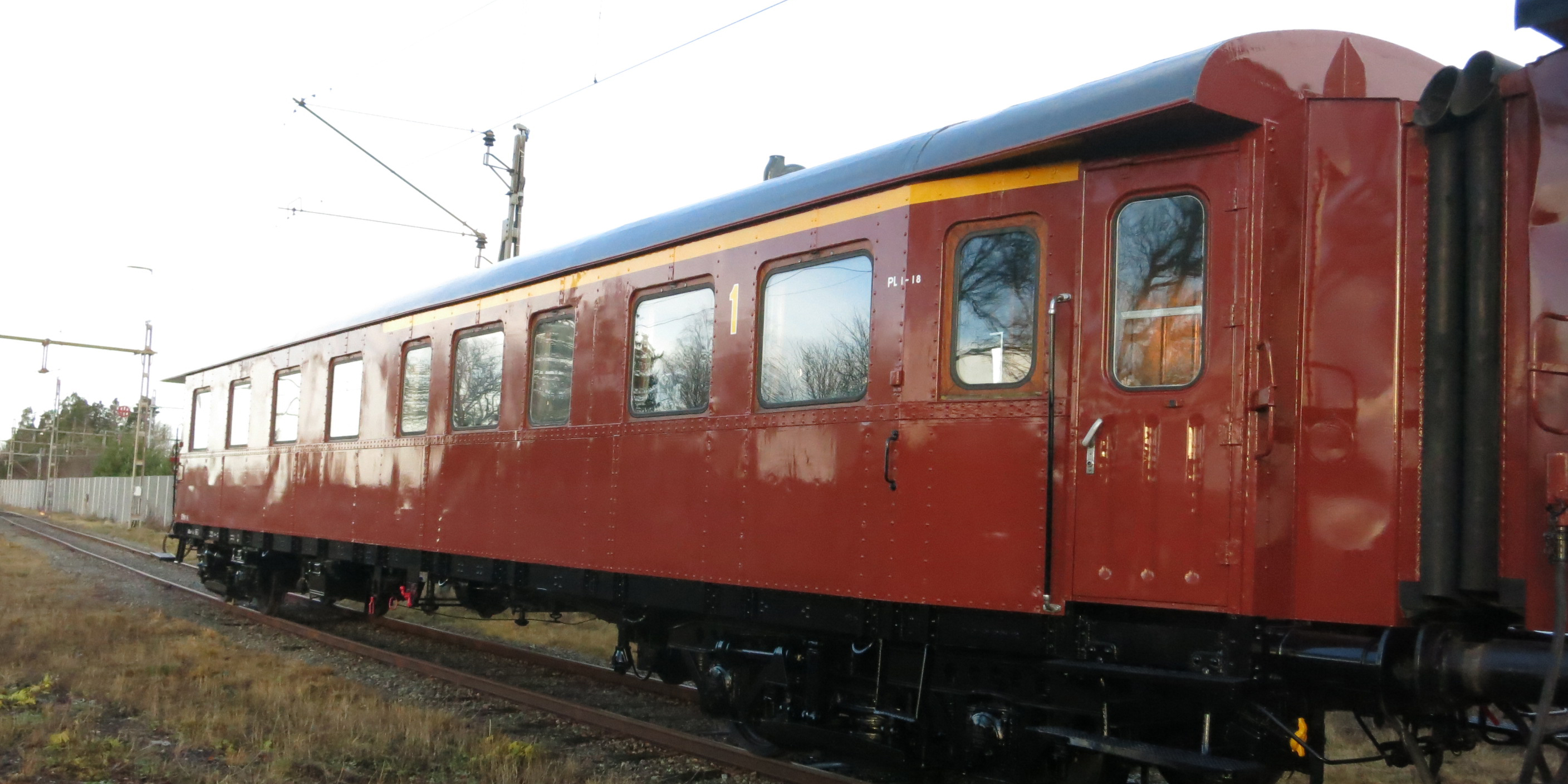 Rust red passenger car with yellow stripe above the windows connected last in line of carriages.