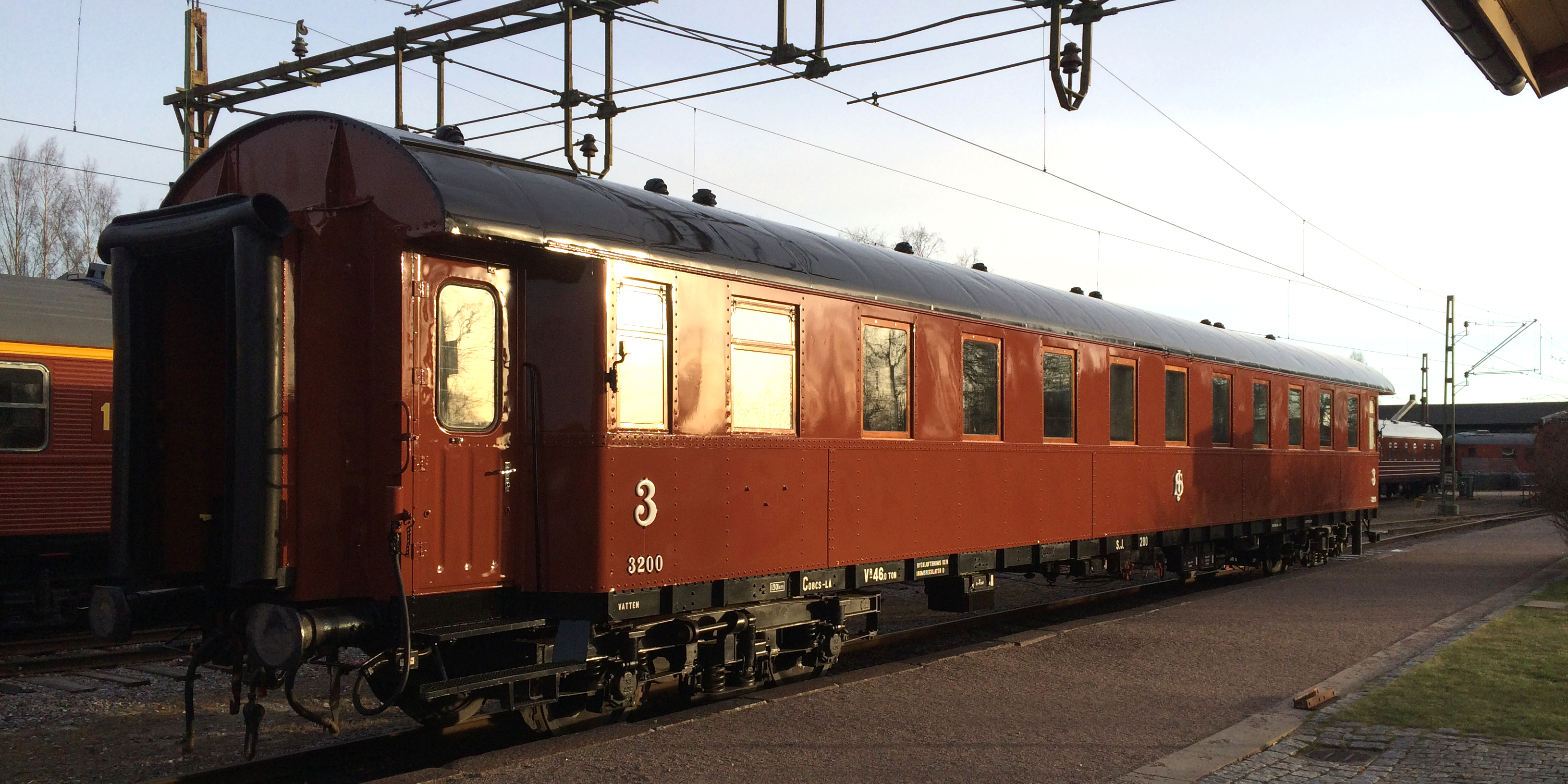 Rust red passenger car with yellow stripes above the windows placed in the station area.