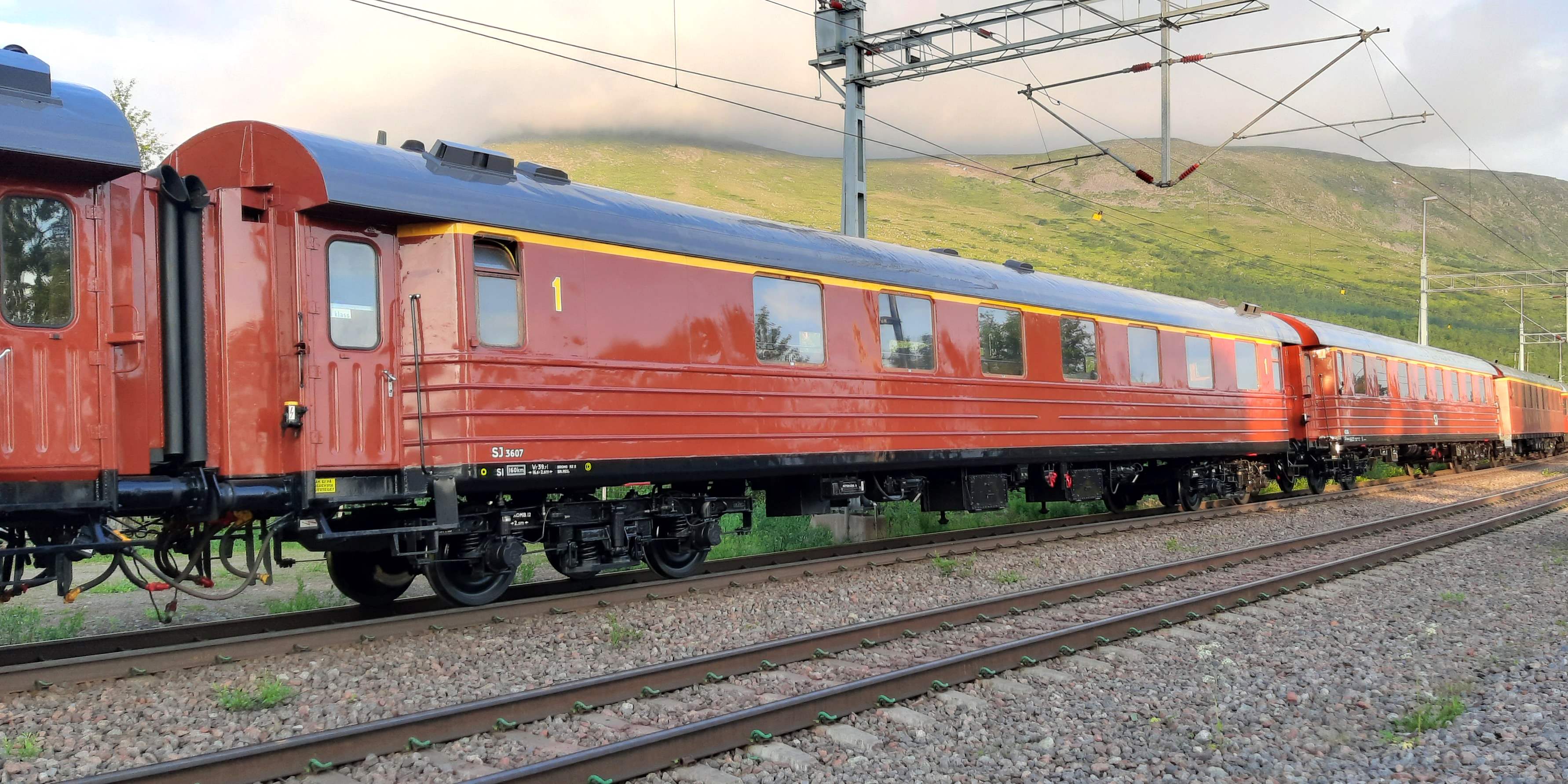Rust red passenger car connected between other cars.