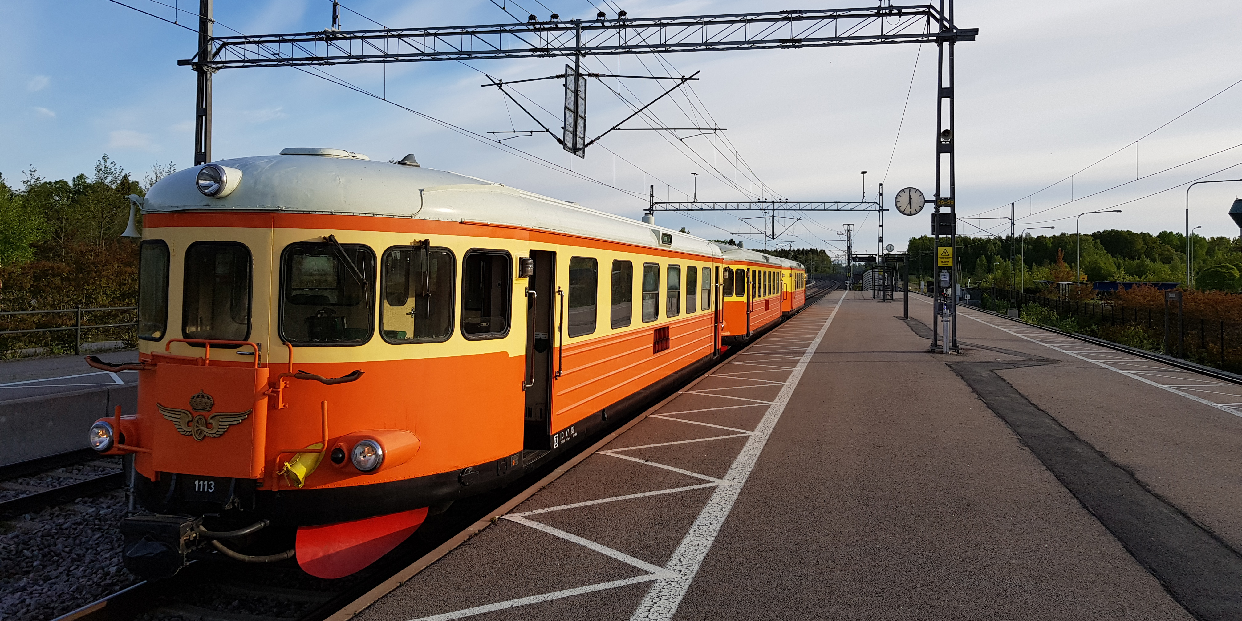 Orange-yellow railbus with several carriages parked at the platform.