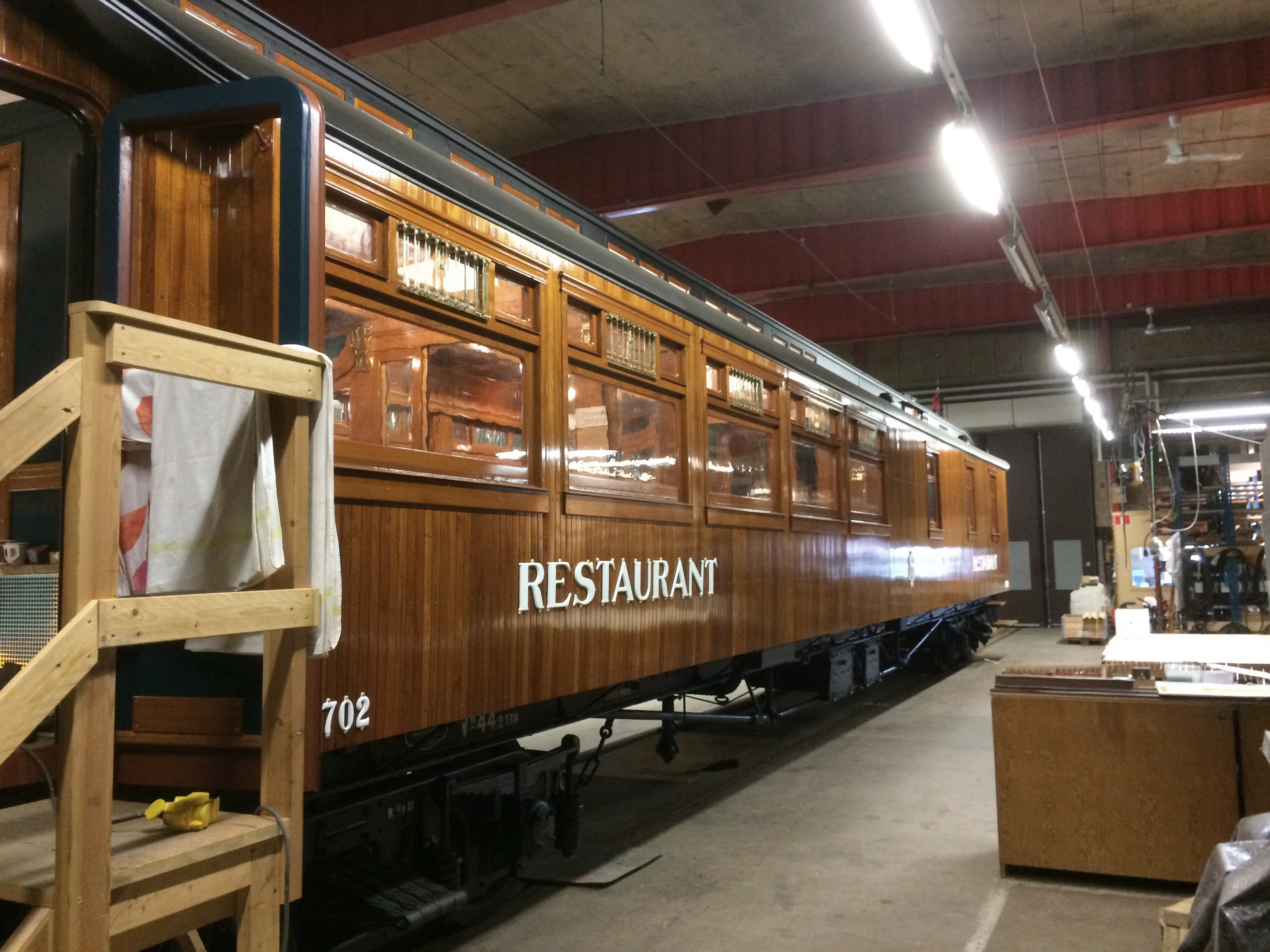 Wood-panelled train carriage in train hall with the word Restaurant on the side. Stairs lead into the carriage for visitors.