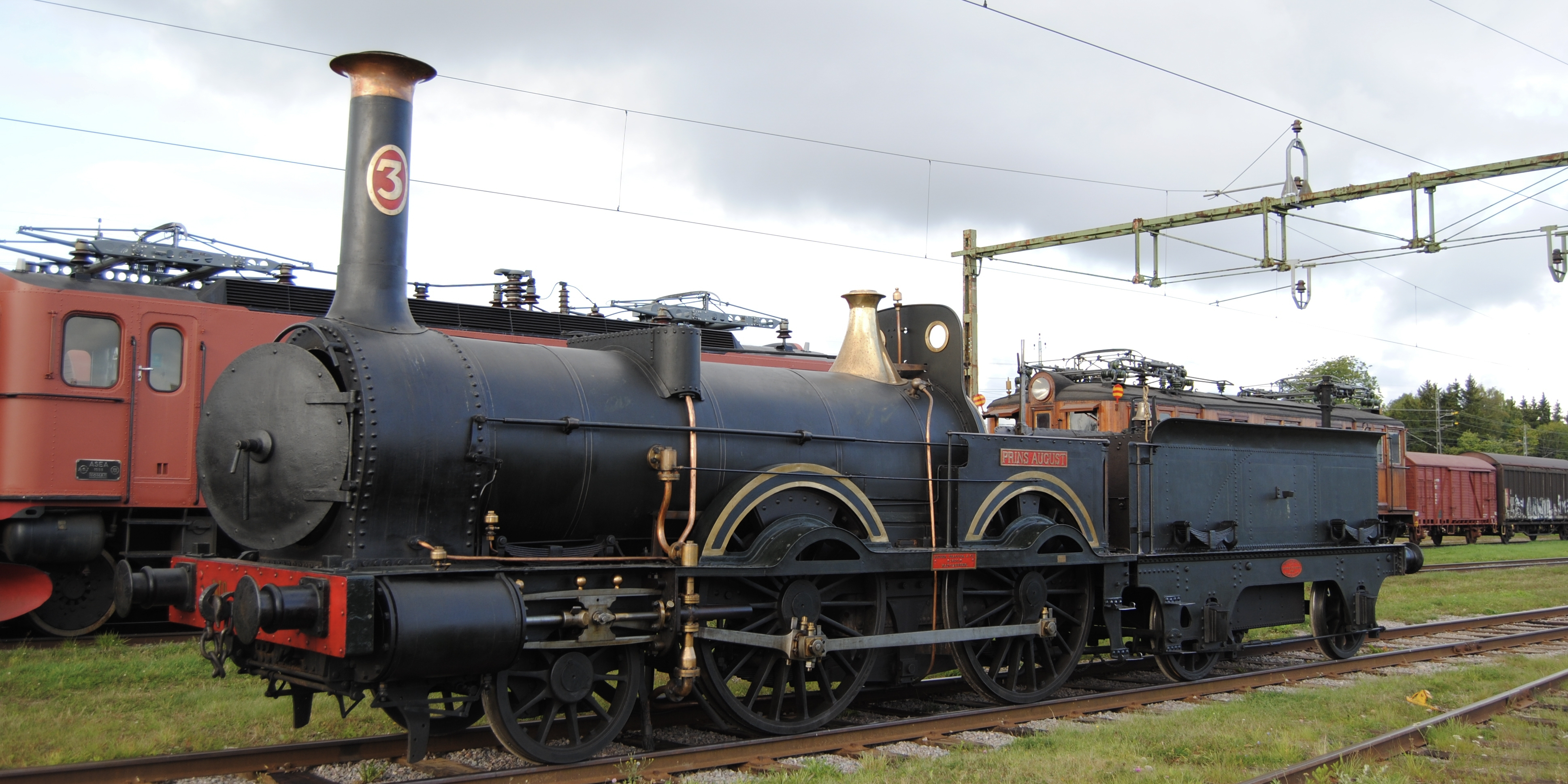The black steam locomotive Prins August from 1956 stands on a track surrounded by green grass.