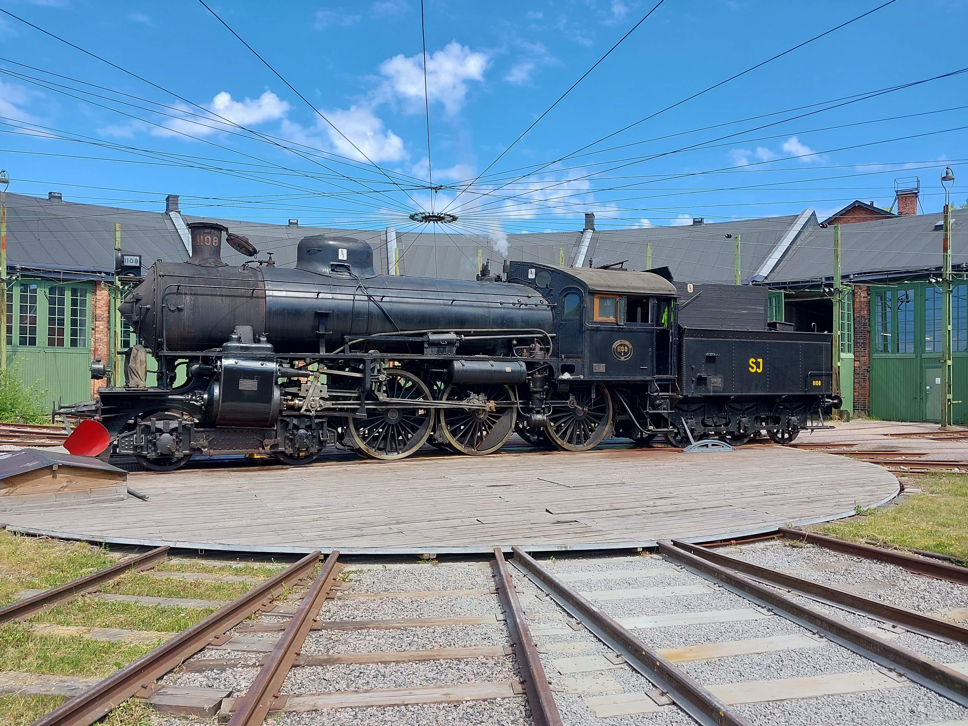 A black steam engine from 1911 is placed in front of its round house.