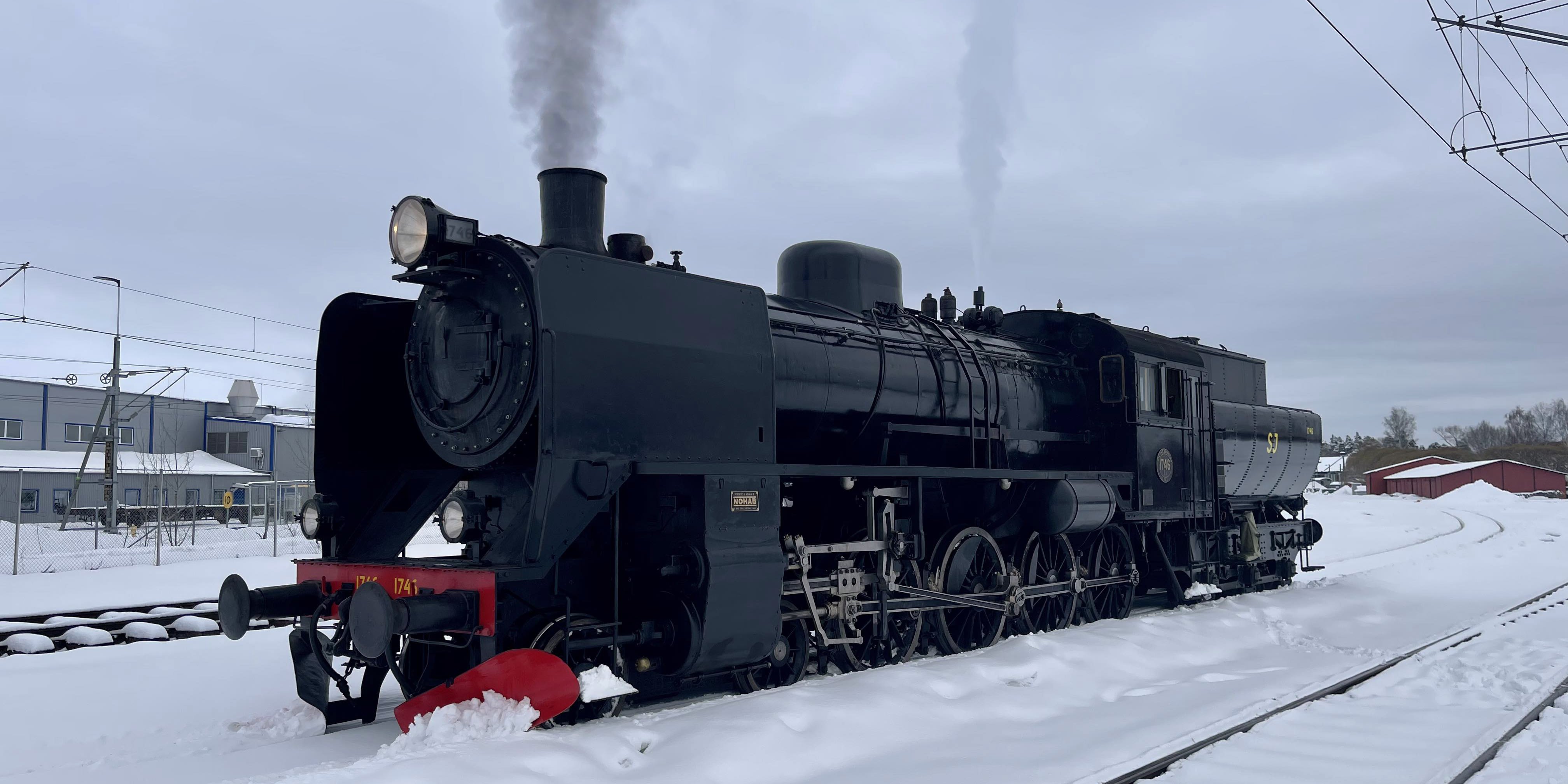 A lone locomotive standing on rails in a winter landscape with smoke rising from the chimney.