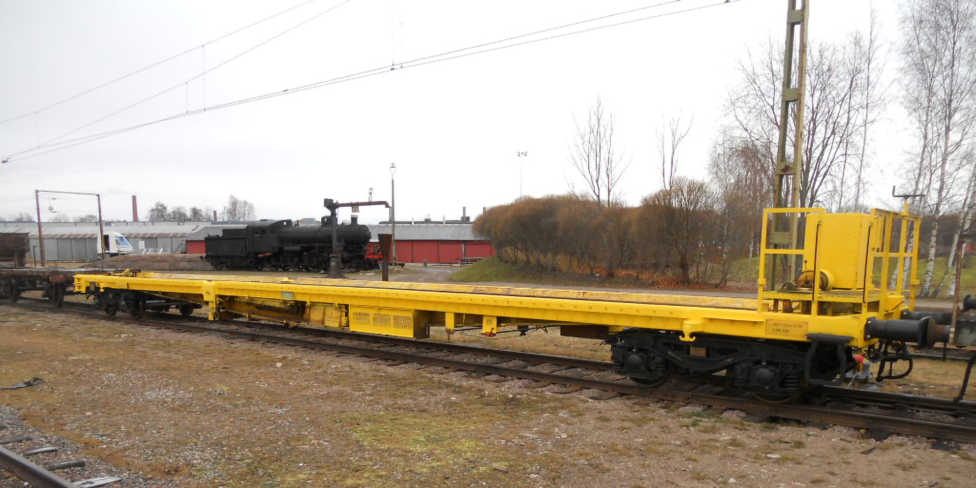 A yellow and flat open freight wagon stands on a track on a grey autumn day.