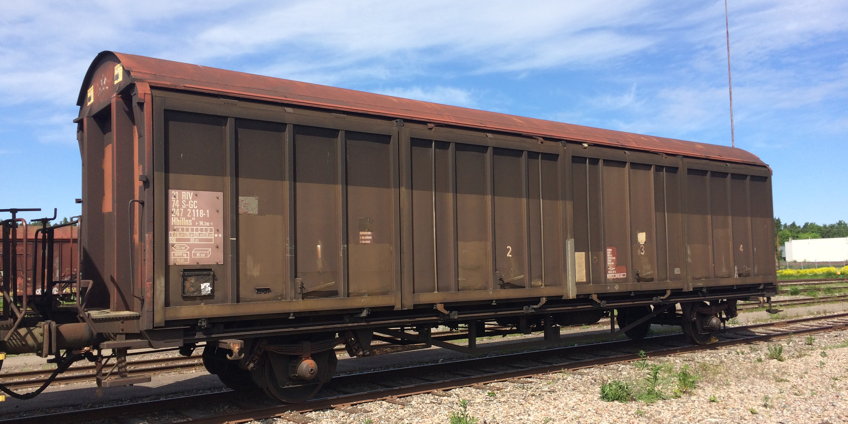 A closed stationary brown freight car with a clear blue sky in the background.