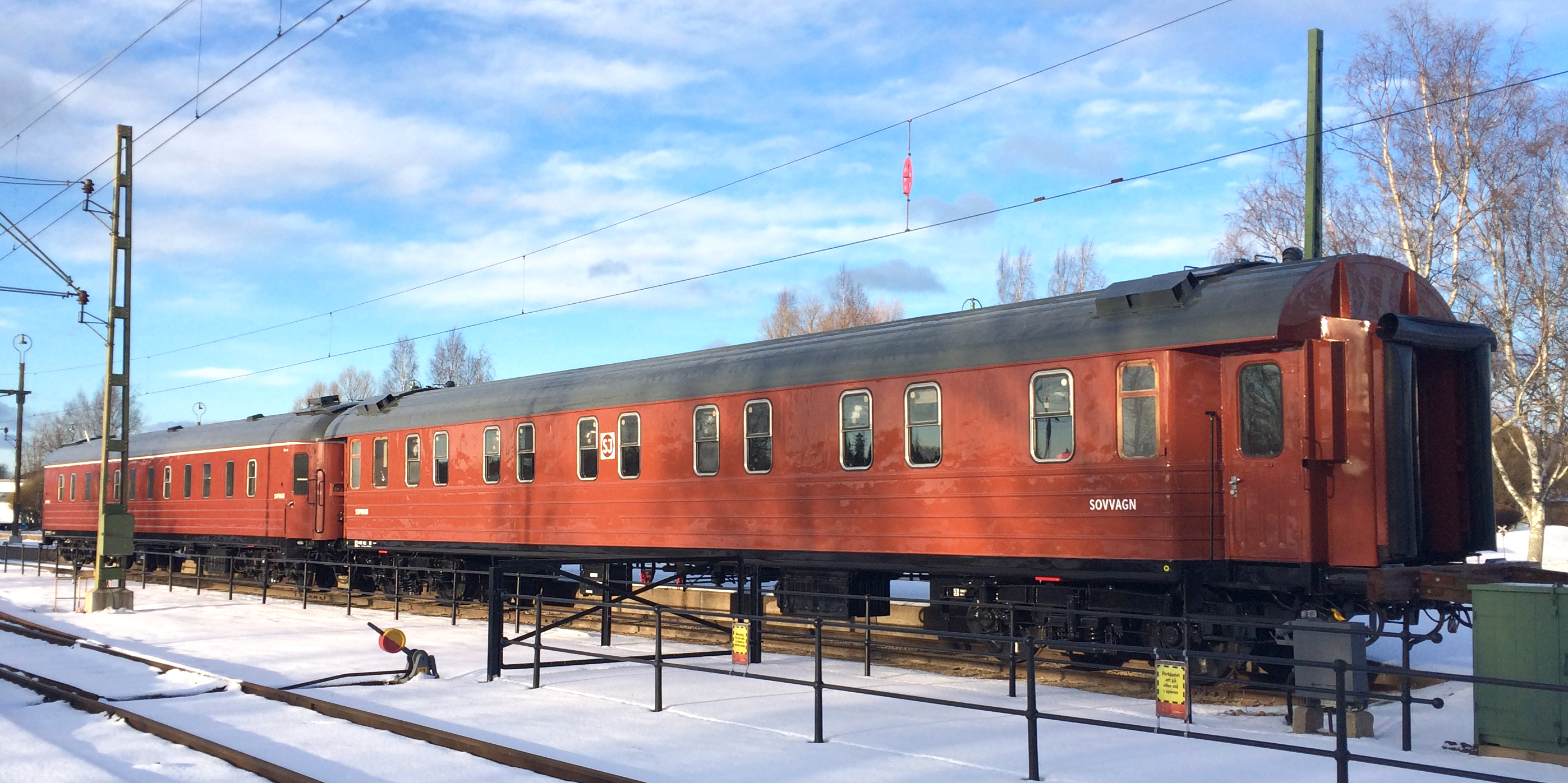 Two red train carriages stationary on tracks with snow-covered ground.