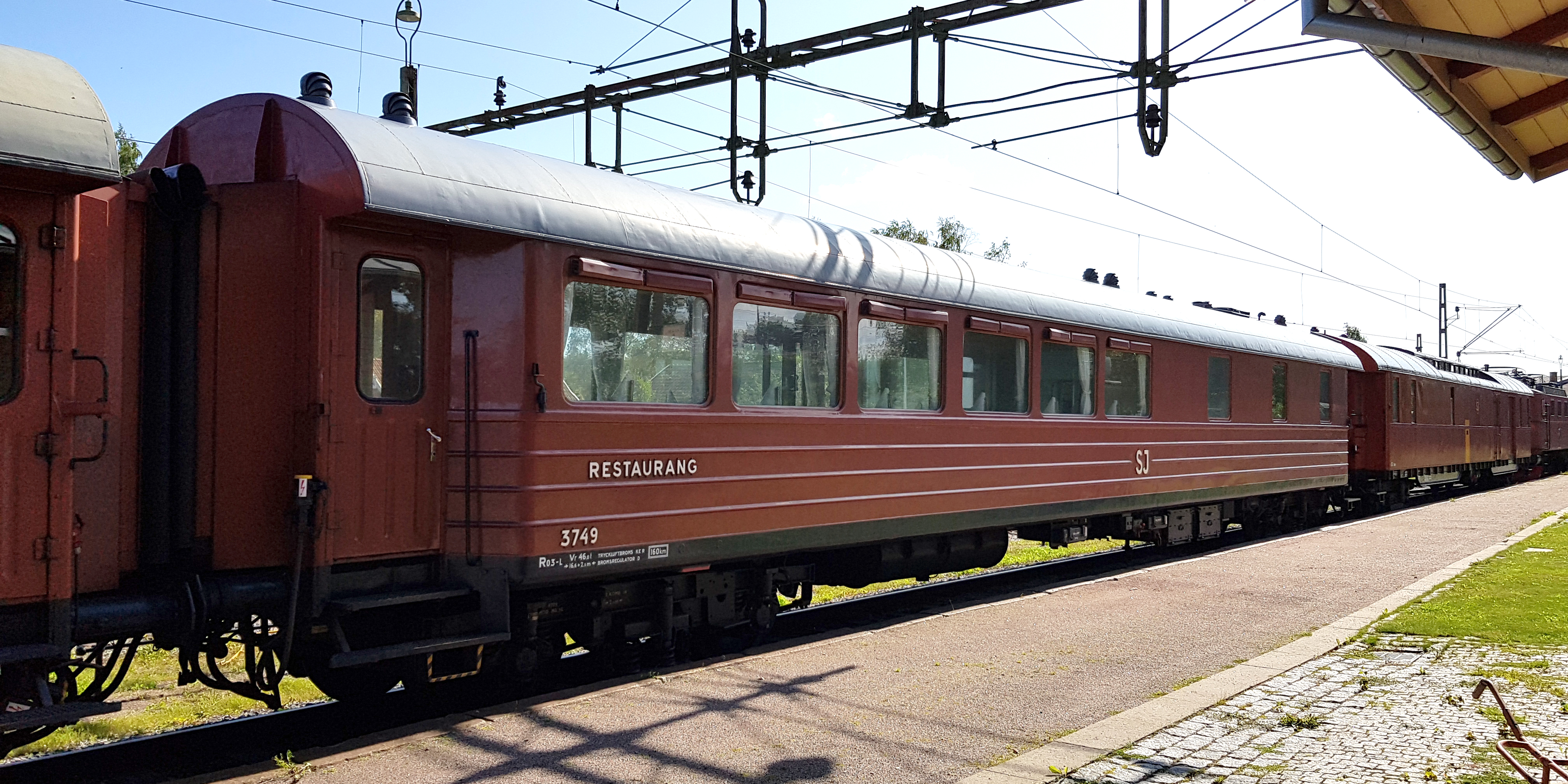 Rust red passenger car connected between other carriages at the platform.